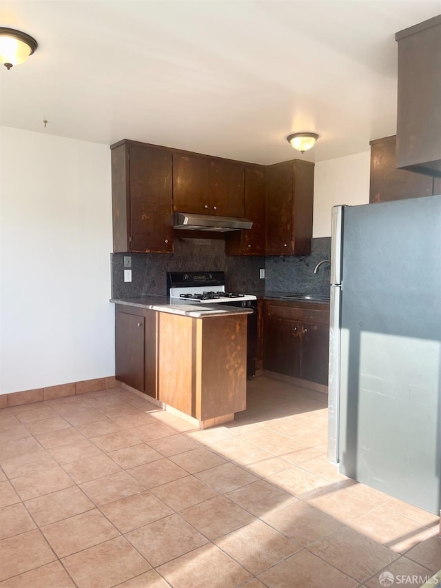 kitchen with under cabinet range hood, backsplash, freestanding refrigerator, gas range gas stove, and dark countertops