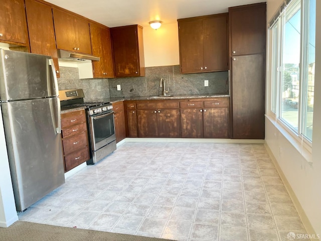 kitchen featuring appliances with stainless steel finishes, a sink, under cabinet range hood, and tasteful backsplash