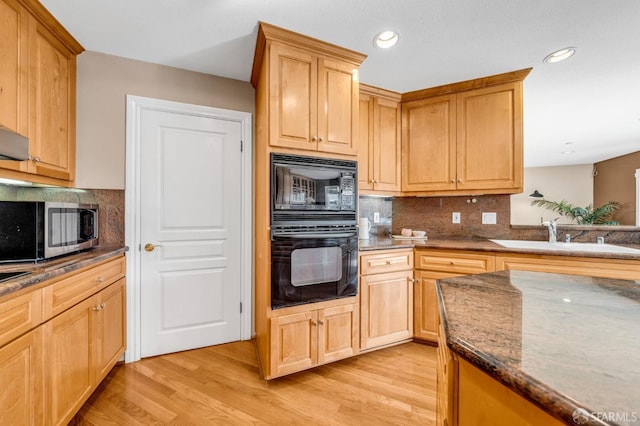 kitchen with light wood-type flooring, a sink, stainless steel microwave, black microwave, and decorative backsplash