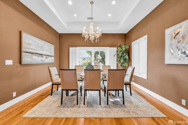 dining area with visible vents, baseboards, a tray ceiling, an inviting chandelier, and wood finished floors