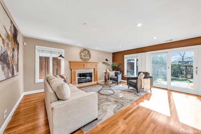 living room with wood finished floors, visible vents, baseboards, recessed lighting, and a glass covered fireplace