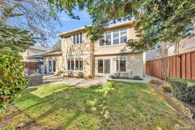 back of house with stucco siding, a lawn, a fenced backyard, and a patio area