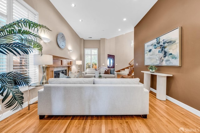 living room with a glass covered fireplace, light wood-style flooring, stairway, and baseboards