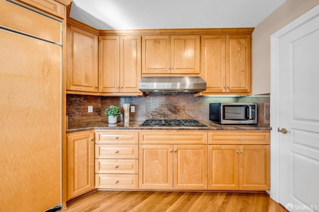 kitchen featuring light wood-type flooring, stainless steel microwave, gas cooktop, and wall chimney range hood