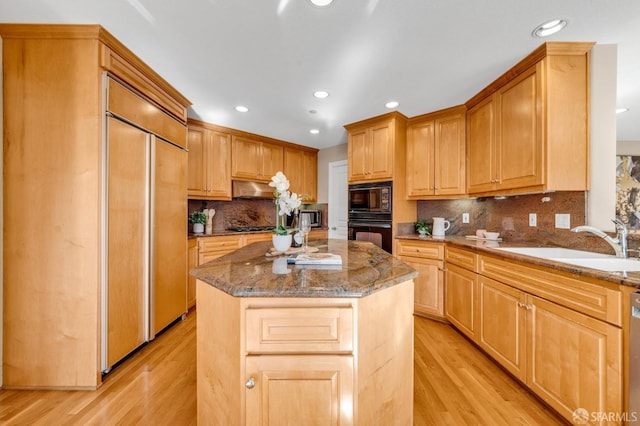 kitchen featuring light wood finished floors, a center island, stone counters, black appliances, and a sink