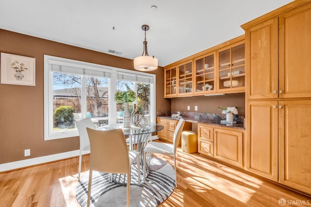 dining room featuring light wood finished floors, visible vents, built in desk, and baseboards