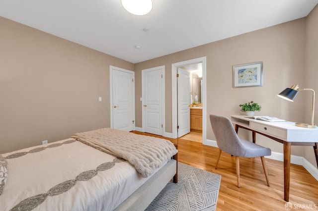 bedroom featuring baseboards, ensuite bath, and light wood finished floors