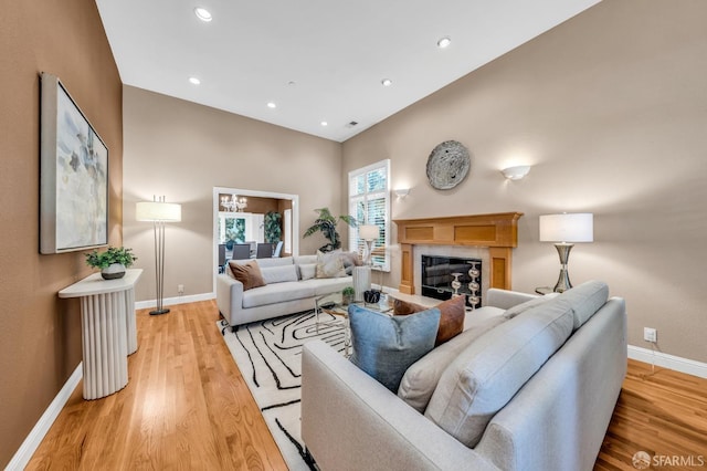 living area featuring a glass covered fireplace, baseboards, light wood-style flooring, and recessed lighting