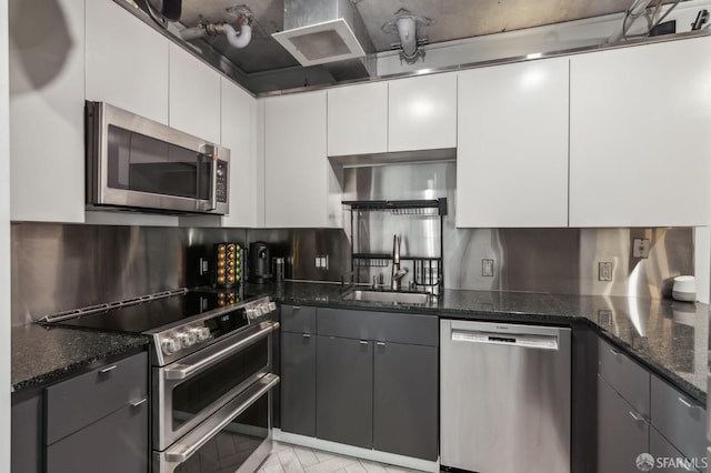 kitchen with gray cabinets, appliances with stainless steel finishes, white cabinetry, sink, and dark stone counters