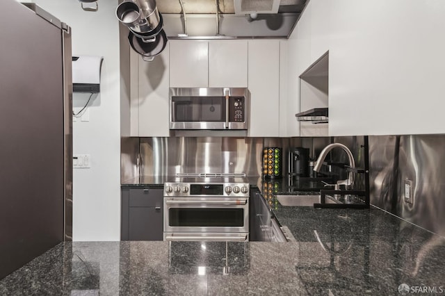 kitchen with appliances with stainless steel finishes, sink, white cabinets, backsplash, and dark stone counters