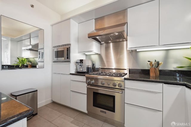 kitchen featuring dark stone countertops, white cabinetry, wall chimney range hood, and appliances with stainless steel finishes