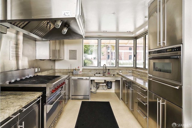 kitchen with light stone countertops, appliances with stainless steel finishes, vaulted ceiling, sink, and range hood