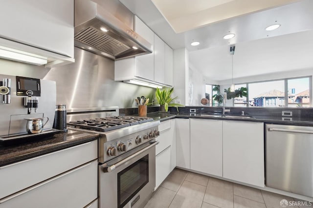 kitchen with dark stone counters, white cabinets, sink, wall chimney exhaust hood, and stainless steel appliances