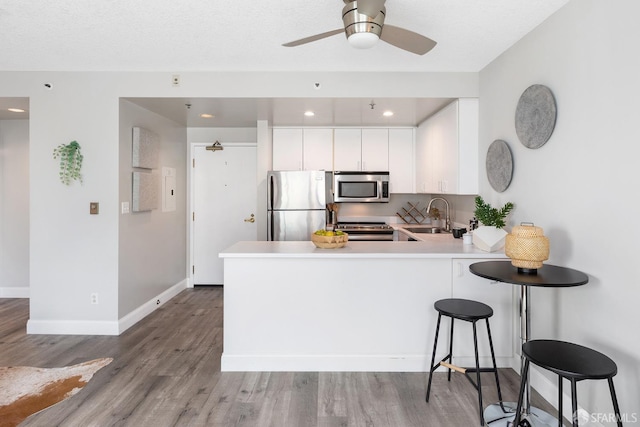 kitchen featuring appliances with stainless steel finishes, white cabinetry, kitchen peninsula, light wood-type flooring, and sink