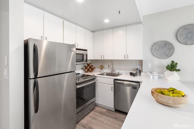 kitchen featuring light wood-type flooring, stainless steel appliances, light countertops, and a sink