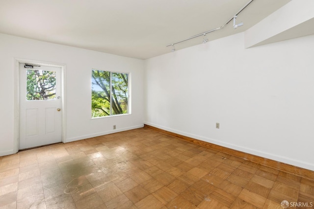 spare room featuring track lighting and baseboards