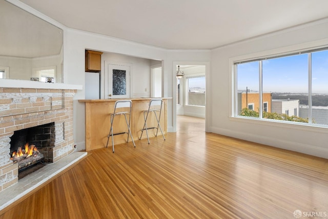 unfurnished living room featuring a brick fireplace, baseboards, ornamental molding, and light wood-style floors