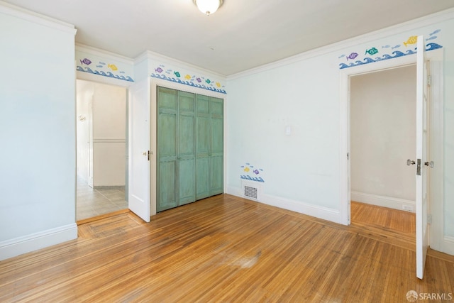 unfurnished bedroom featuring light wood-type flooring, crown molding, baseboards, and a closet