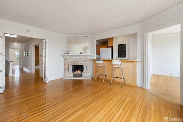 unfurnished living room with light wood-style floors, a brick fireplace, baseboards, and crown molding