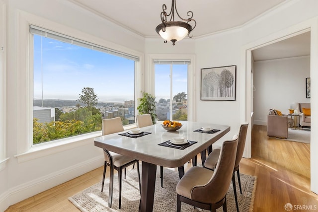 dining area with light wood-style flooring, ornamental molding, and baseboards