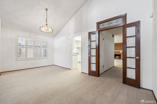 spare room featuring high vaulted ceiling, a notable chandelier, a fireplace, and carpet flooring