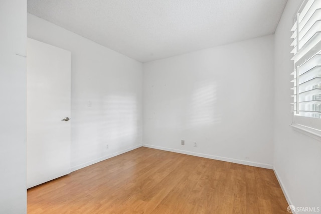 empty room featuring baseboards, a textured ceiling, and light wood finished floors