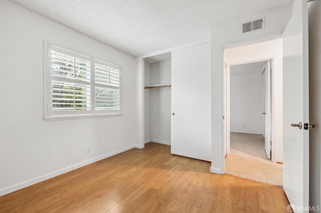 unfurnished bedroom with light wood finished floors, visible vents, a textured ceiling, and a closet