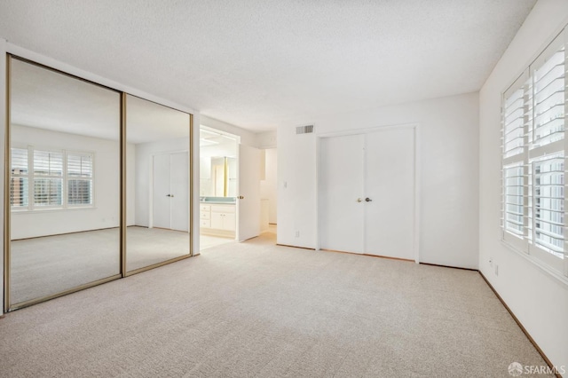 unfurnished bedroom with visible vents, multiple closets, carpet floors, a textured ceiling, and ensuite bath