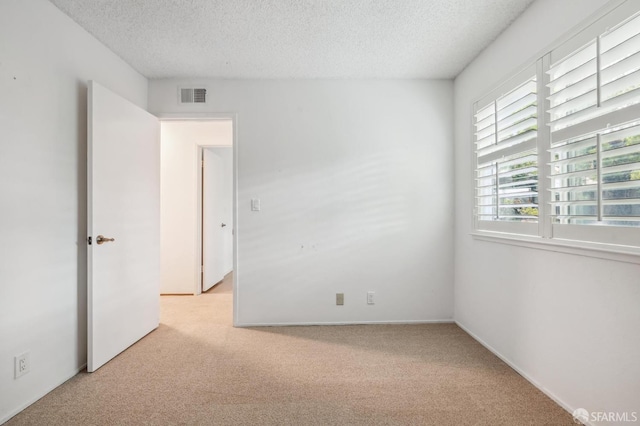 unfurnished room with carpet, visible vents, and a textured ceiling