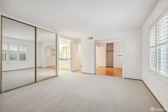 unfurnished bedroom with visible vents, multiple windows, a textured ceiling, and carpet flooring