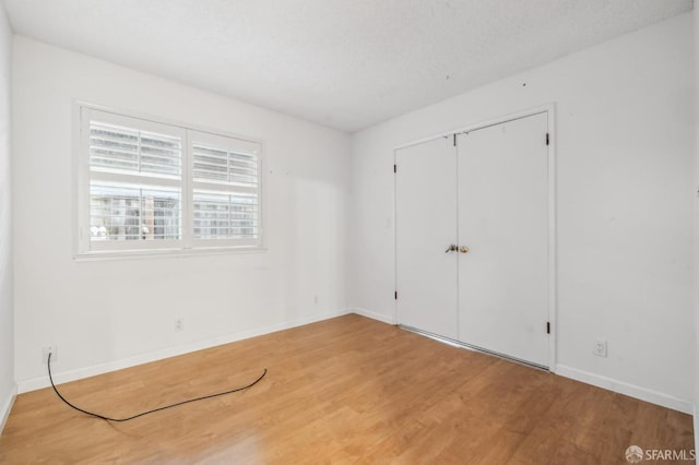 unfurnished bedroom with wood finished floors, baseboards, a closet, and a textured ceiling