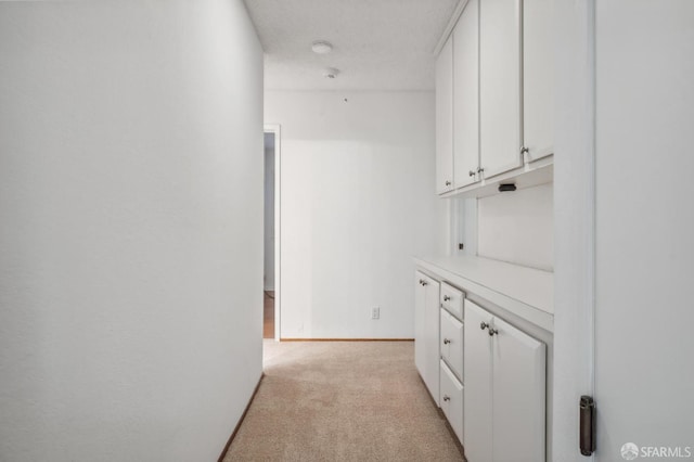 corridor with a textured ceiling, baseboards, and light carpet