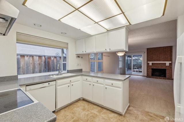 kitchen with light carpet, a peninsula, white dishwasher, white cabinets, and a sink