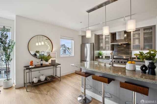 kitchen featuring wall chimney range hood, freestanding refrigerator, a breakfast bar, and light wood-type flooring