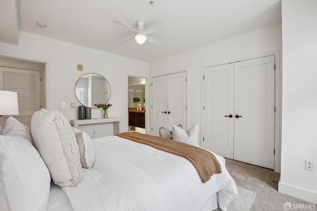 bedroom with ensuite bathroom, ceiling fan, two closets, and light carpet