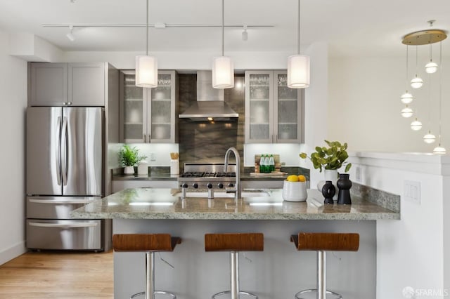 kitchen with wall chimney range hood, a kitchen breakfast bar, track lighting, light stone counters, and freestanding refrigerator