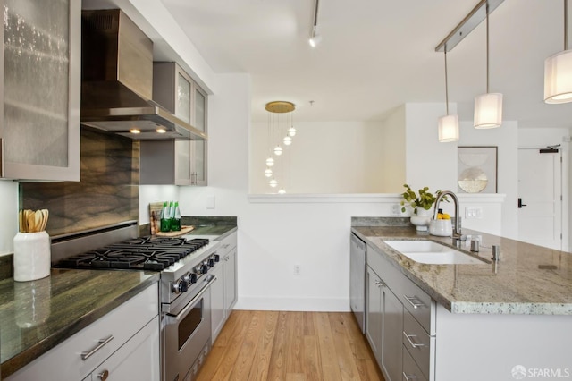 kitchen featuring a sink, wall chimney exhaust hood, stainless steel appliances, a peninsula, and light wood-type flooring