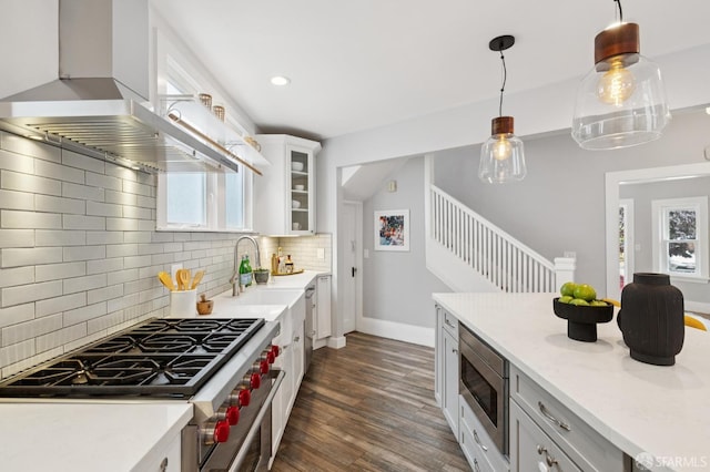 4145 Emerald St, Oakland, CA 94609 - kitchen with wall chimney range hood, stainless steel appliances, dark wood-style flooring, decorative backsplash, and glass insert cabinets