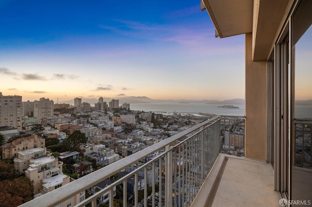 balcony at dusk featuring a water and mountain view