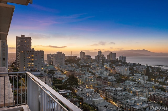 balcony at dusk featuring a water and mountain view