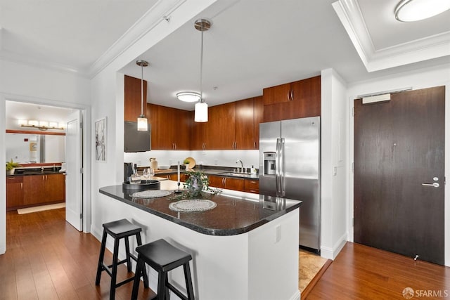 kitchen featuring a kitchen breakfast bar, wood-type flooring, stainless steel fridge, crown molding, and pendant lighting