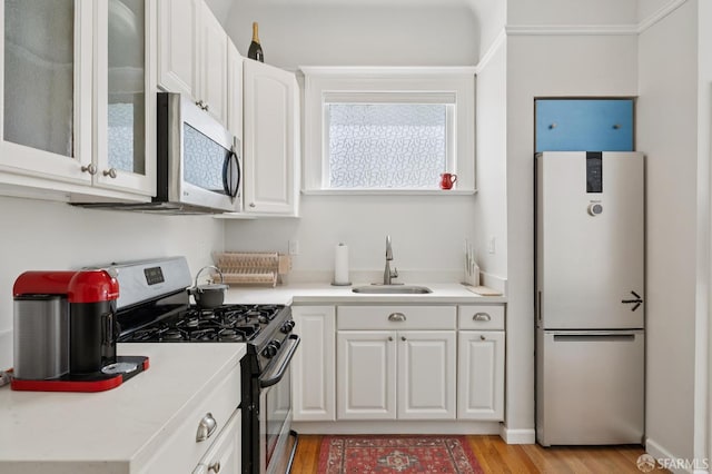 1932 Fell St Unit 1, San Francisco, CA 94117 - kitchen featuring stainless steel appliances, a sink, white cabinetry, light wood finished floors, and glass insert cabinets
