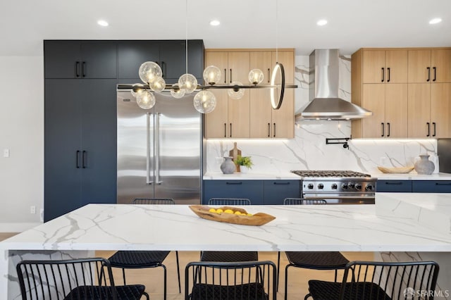 kitchen with light stone counters, wall chimney range hood, high quality appliances, and a kitchen island