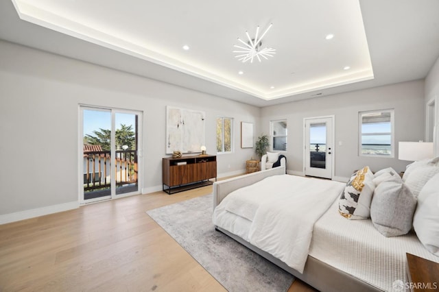 bedroom with light hardwood / wood-style flooring, a tray ceiling, and access to outside