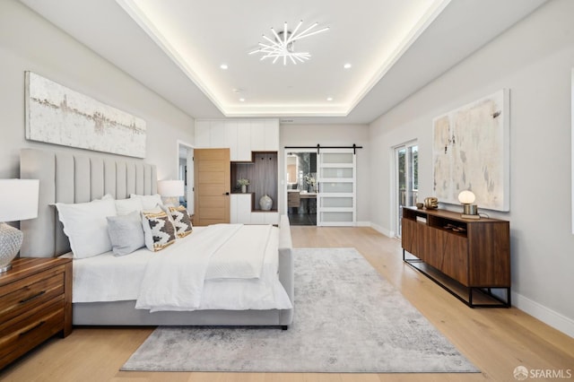 bedroom featuring a tray ceiling, a barn door, and light hardwood / wood-style floors