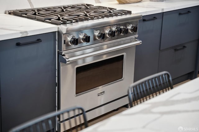 kitchen featuring high end stainless steel range oven, blue cabinets, and light stone counters