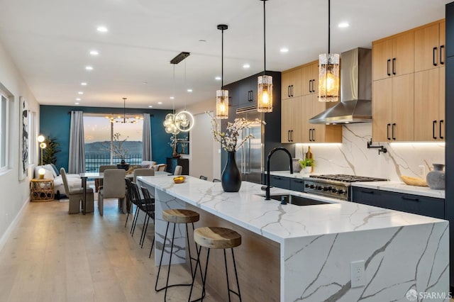 kitchen with light stone counters, decorative light fixtures, light brown cabinets, and wall chimney range hood