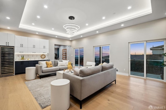 living room featuring a tray ceiling, light hardwood / wood-style flooring, and beverage cooler