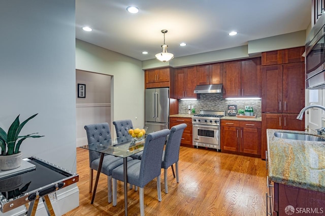 kitchen featuring pendant lighting, dark stone counters, light hardwood / wood-style floors, sink, and premium appliances