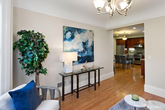 living area with ornamental molding, a chandelier, and light hardwood / wood-style floors